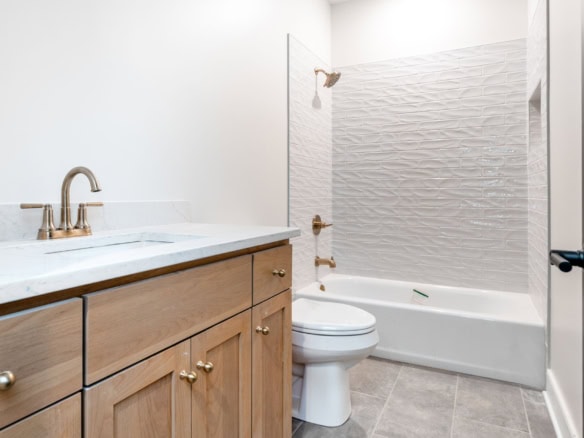 Bathroom with wooden vanity, bathtub, and textured wall tiles.