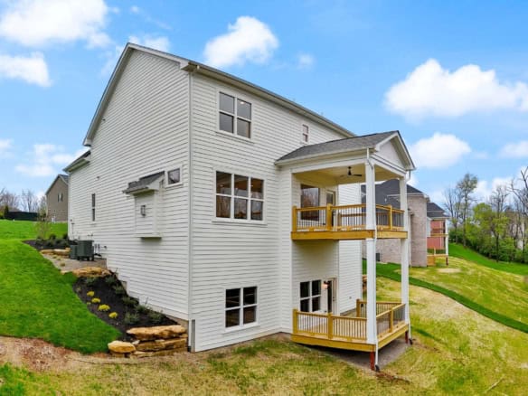 New white house with two wooden balconies on a grassy hill under a blue sky.