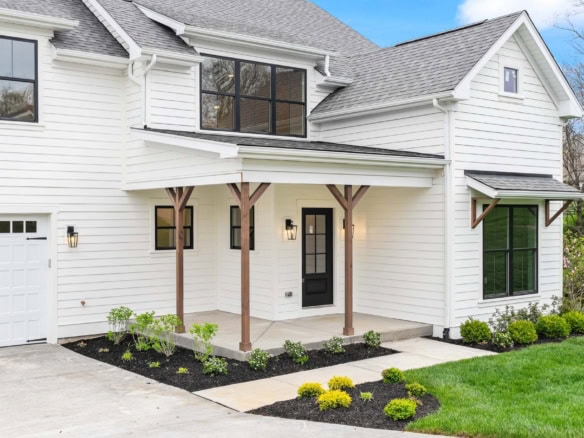 New white house with front porch, black door, and landscaped yard.