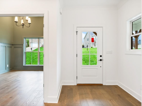 Bright entryway with white walls, wooden floors, and large windows showing green yard.