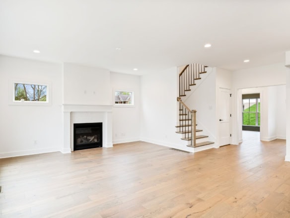 Bright, spacious living room with white walls, hardwood floors, and staircase.