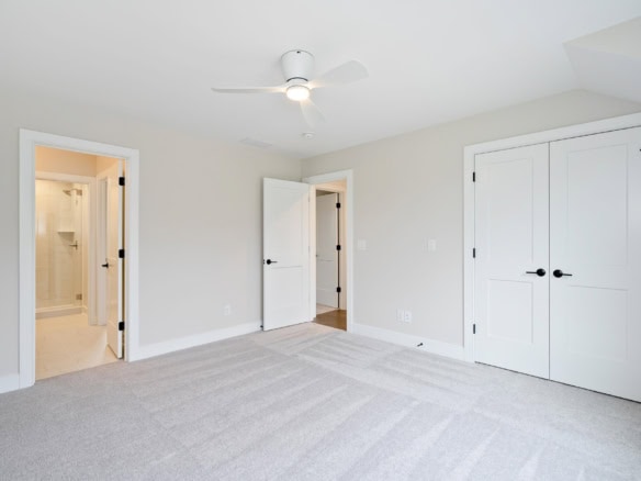 Interior of a modern bedroom with white walls, carpet flooring, and a ceiling fan.