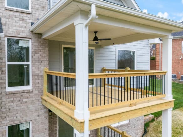 New wooden balcony with black metal railing on residential home.