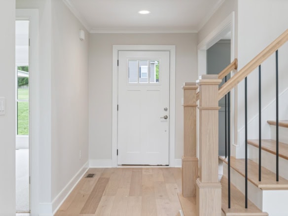 Bright and welcoming home entry with white door and natural wood staircase.