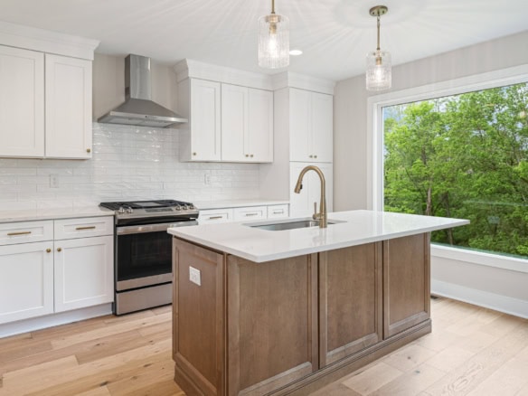 Bright kitchen featuring white cabinetry, a central island, and large window overlooking greenery.