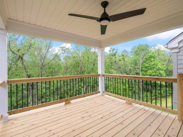 Balcony with ceiling fan overlooking lush green trees and blue sky.