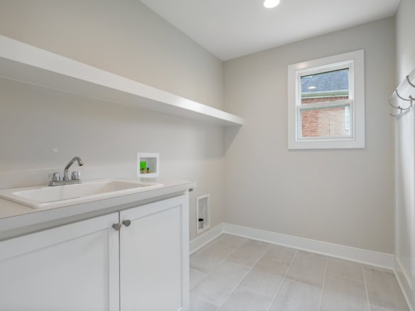 Bright laundry room with white cabinetry and a window.