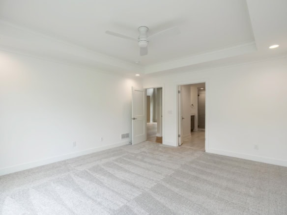 A bright, spacious living room with white walls, ceiling fan, and carpeted floor.