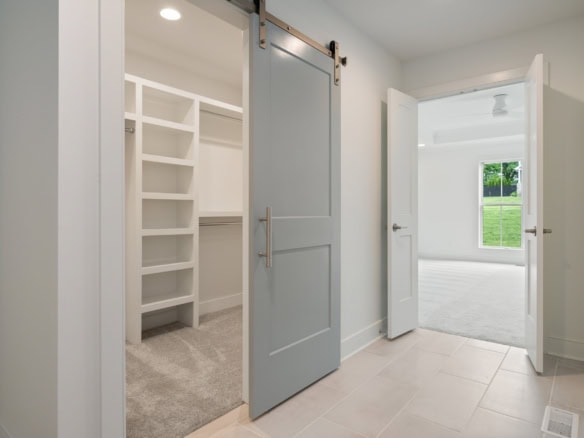 Interior view of a modern closet with sliding barn door and adjacent bedroom.