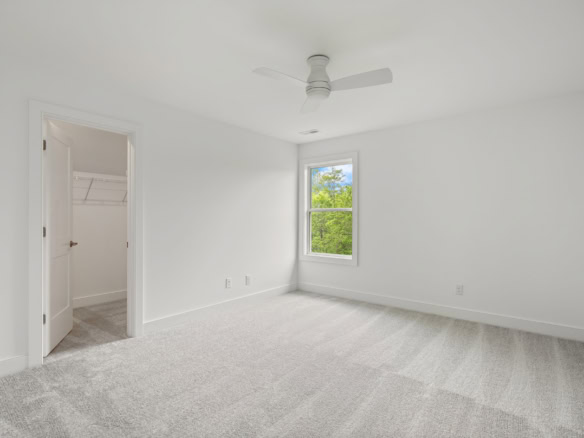 Bright, empty bedroom with white walls and carpet, window view.