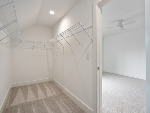 Interior view of a spacious walk-in closet with white walls and carpeted floor.