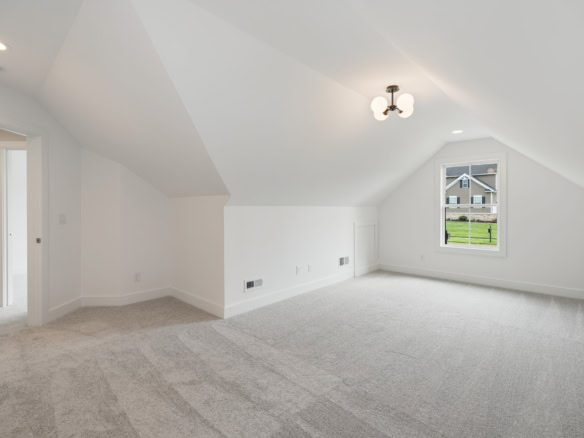 Attic bedroom with window, ceiling light, and white walls in a new home.