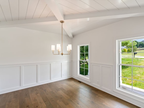 Interior view of a bright, spacious room with white walls, wood flooring, and large windows overlook.