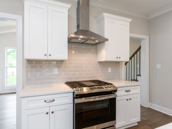 Kitchen featuring white cabinets, a stainless steel stove, and a beige tile backsplash.