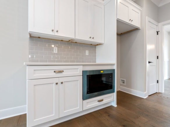 Modern white kitchen cabinets with built-in microwave and gray backsplash.