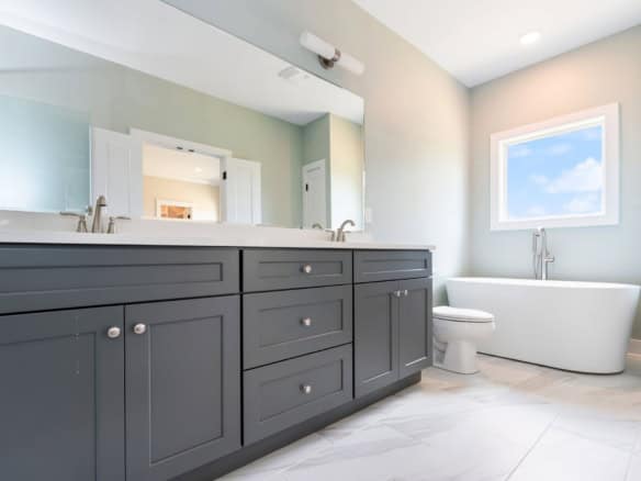 Bright bathroom featuring a double vanity, large mirror, and freestanding bathtub.