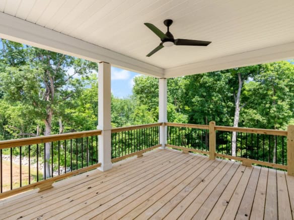 Spacious covered porch with ceiling fan overlooking lush trees.
