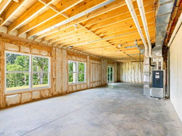 Interior view of a new home under construction with exposed framing and windows.