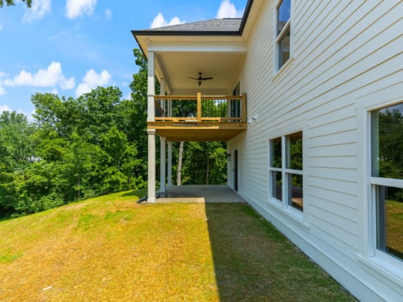 New white house with balcony and large windows in a lush green setting.