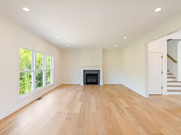 A bright, spacious living room with large windows, hardwood floors, and a fireplace.