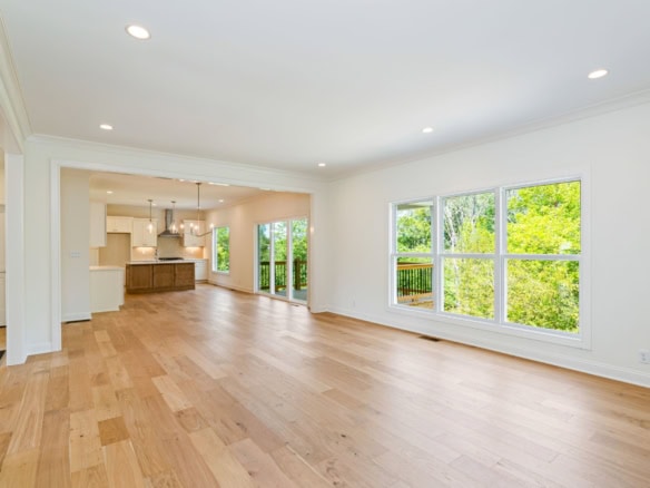 A spacious living area with large windows, hardwood flooring, and an open kitchen in a new home.