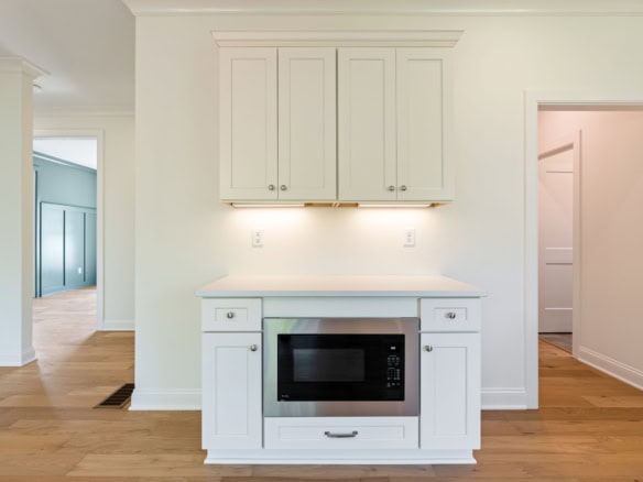 Modern white kitchen cabinetry with microwave and open space.