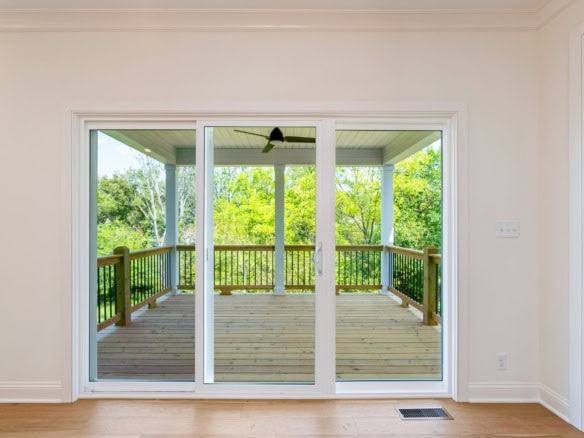 Sliding glass door leading to a wooden deck with green trees in the background.