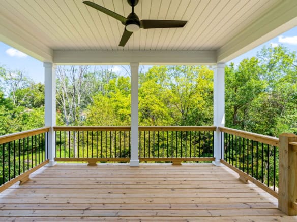 Spacious balcony with wooden flooring and lush green trees in the background.