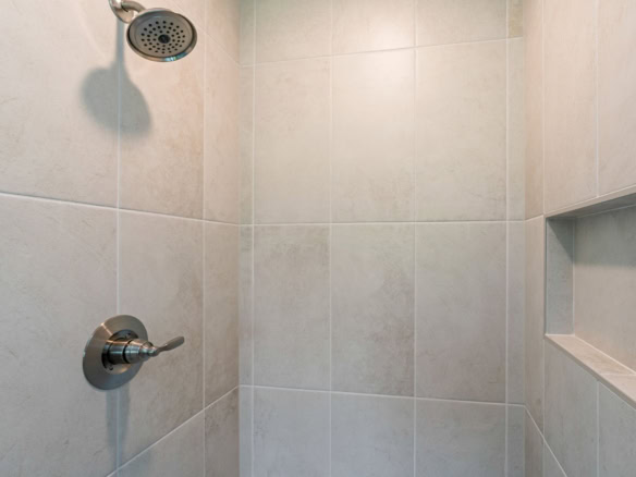 Shower with beige tiles, rainfall showerhead, and built-in niche for toiletries.