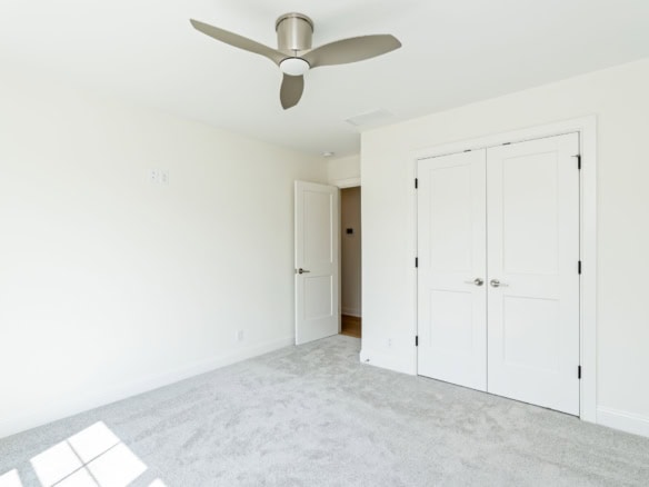 Interior view of a bright, modern bedroom with white walls, closet doors, and a ceiling fan.