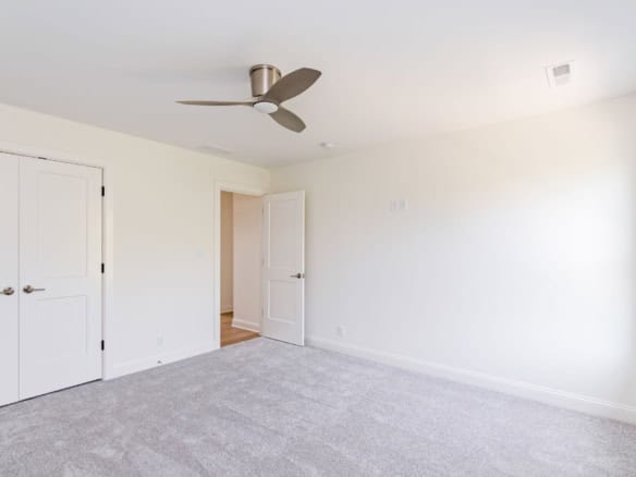 Bright, empty bedroom with white walls and ceiling fan.