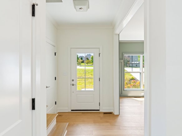Bright entryway with white walls, wooden flooring, and a glass door leading outside.