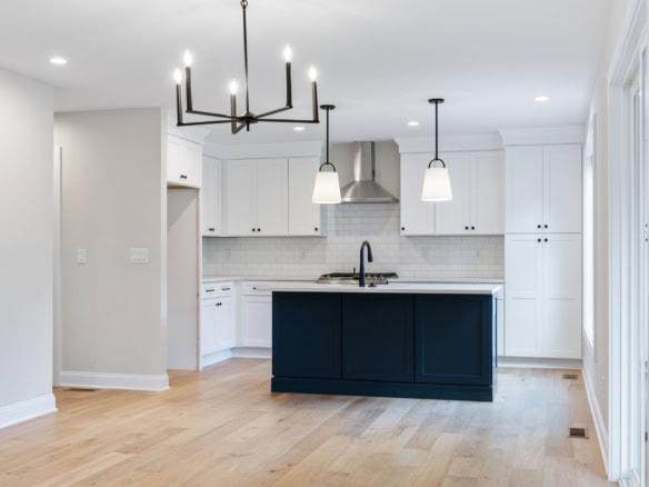 Bright modern kitchen featuring white cabinetry, navy island, and pendant lighting.