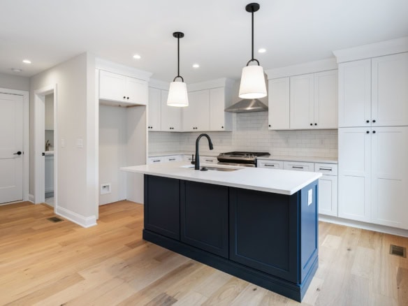Bright modern kitchen featuring white cabinets, a blue island, and pendant lighting.