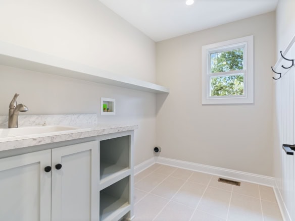 Bright laundry room with white cabinets, window, and tiled floor.