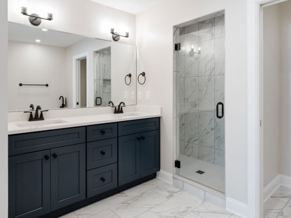 Bathroom with navy vanity, double sinks, and glass shower.