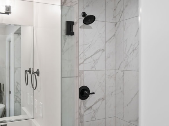 Bathroom shower with marble tiles and black showerhead and controls.