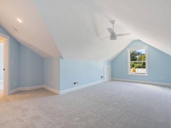 Bright attic bedroom with blue walls, large window, and ceiling fan.