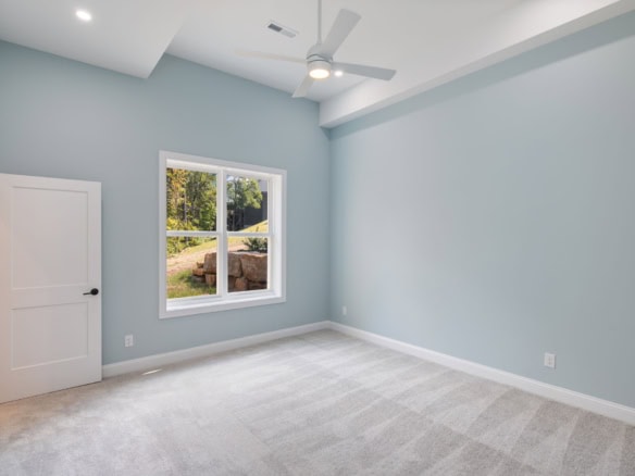 Bright, empty bedroom with large window and ceiling fan.