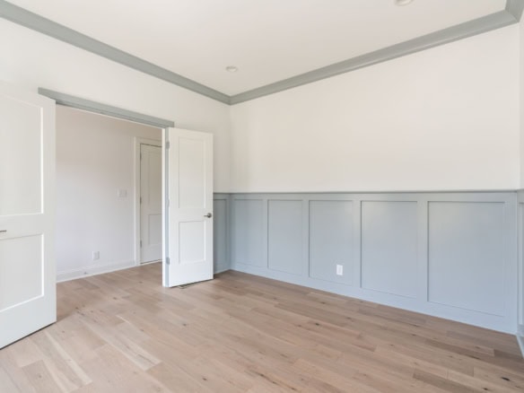 Interior view of a bright, spacious room with white walls and light wood flooring.