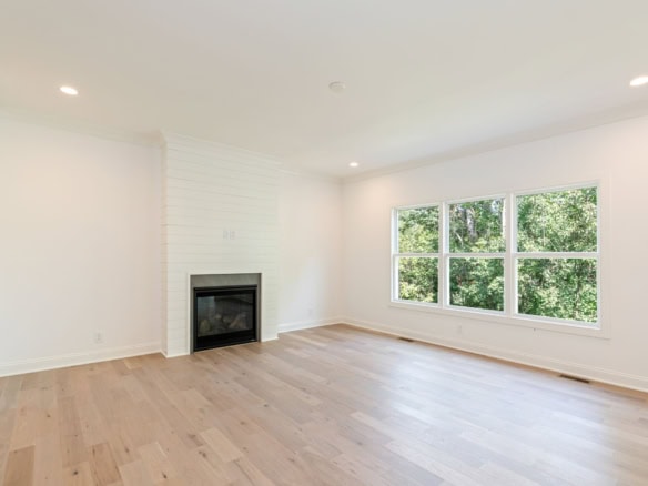 Bright living room featuring large windows, hardwood floors, and a cozy fireplace.