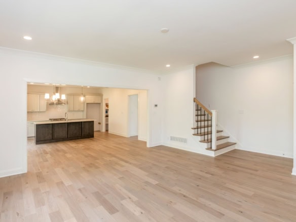 Bright, open-concept living area with white walls, hardwood floors, and staircase.