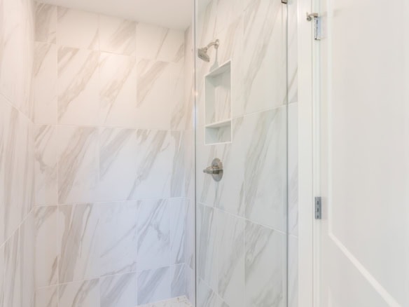 Bathroom shower with marble wall tiles and built-in shelf.