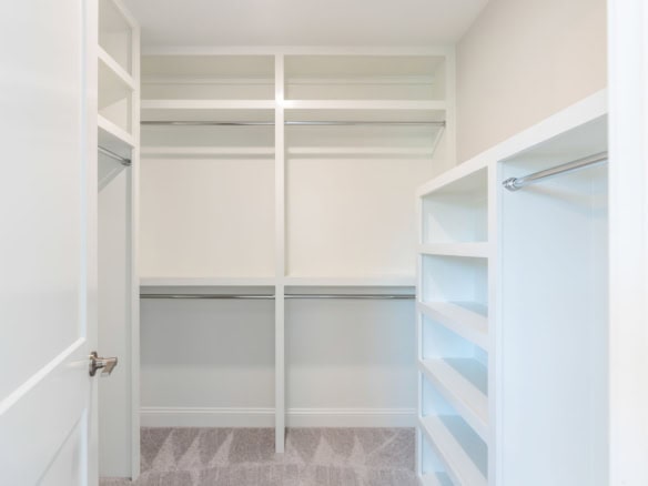 Walk-in closet with white shelves and hanging rods for organized storage.