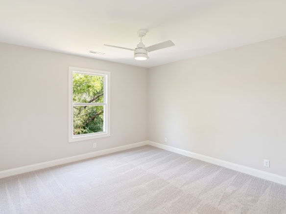 Bright, empty room with white walls, large window, and ceiling fan.