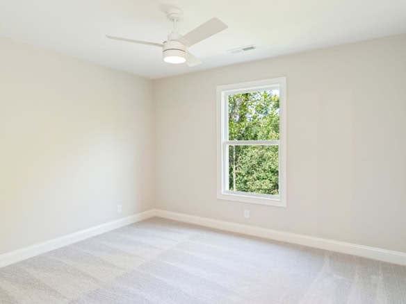 Bright, empty bedroom with white walls, large window, and ceiling fan.