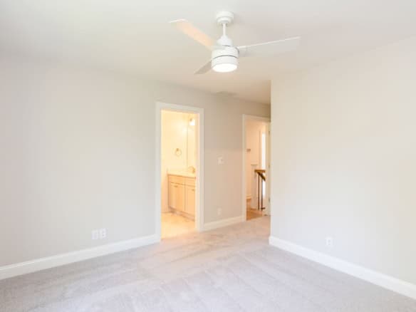 Living room interior with white walls, ceiling fan, and doorway to bathroom.