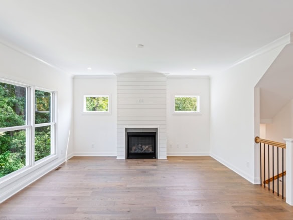Spacious living room with large windows, white walls, and a fireplace.
