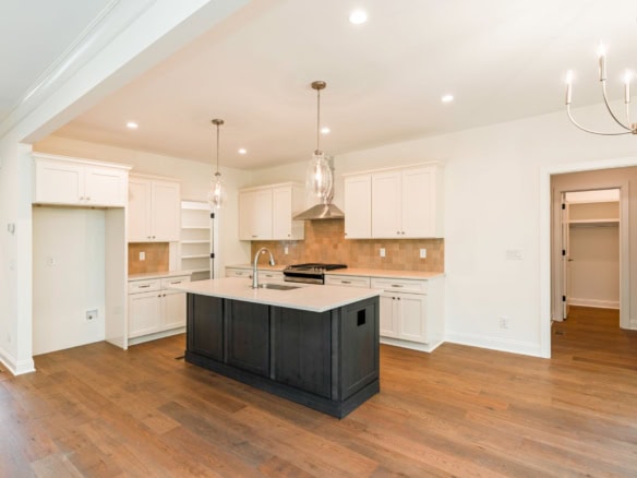 Spacious modern kitchen featuring a central island, white cabinetry, and hardwood floors.