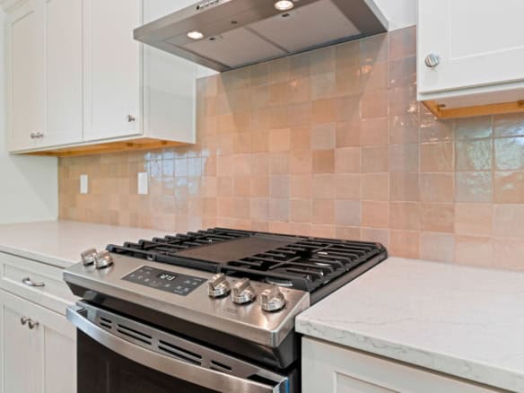 Bright kitchen featuring white cabinets, beige tiled backsplash, and stainless steel gas stove.